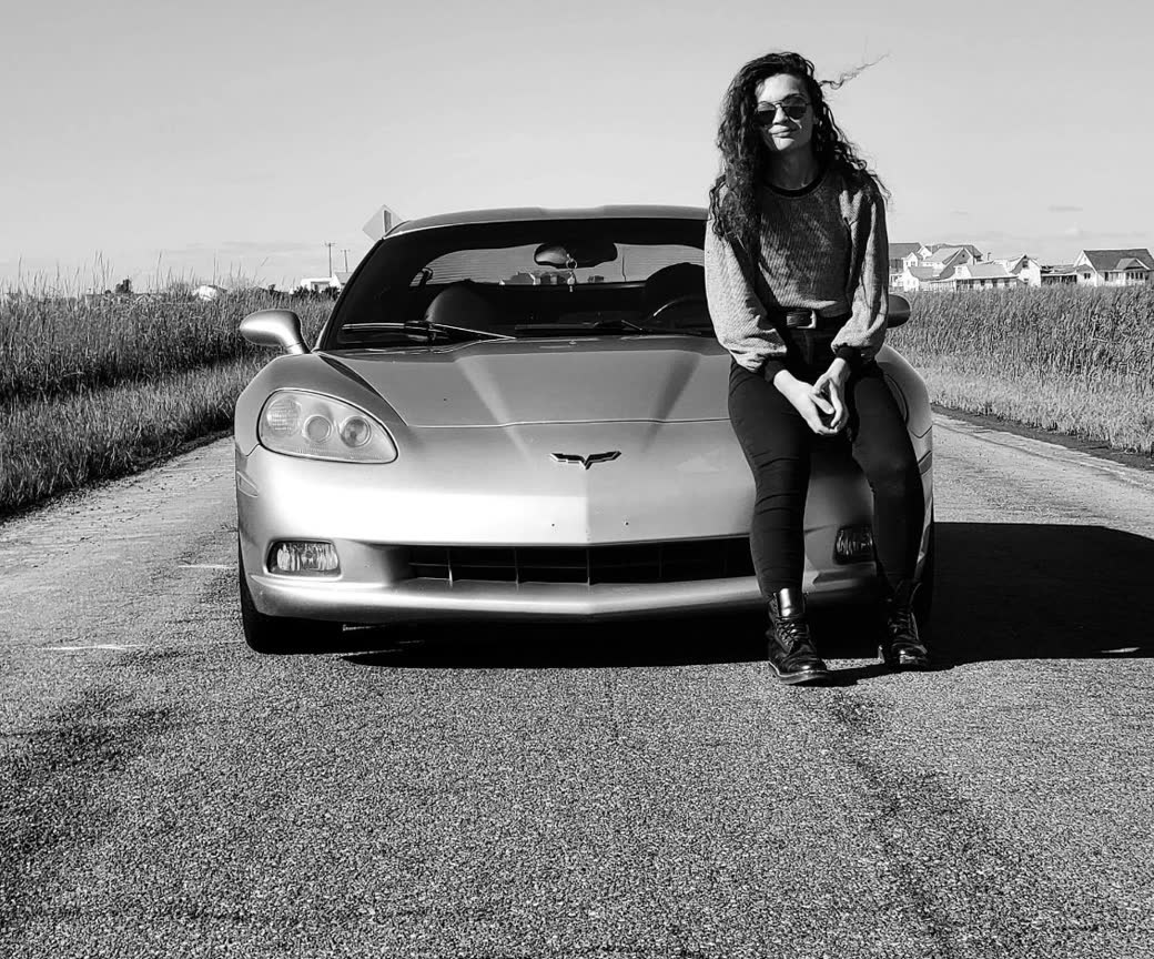 The owner of DEETOE CO. sitting on the hood of a Corvette on a country road