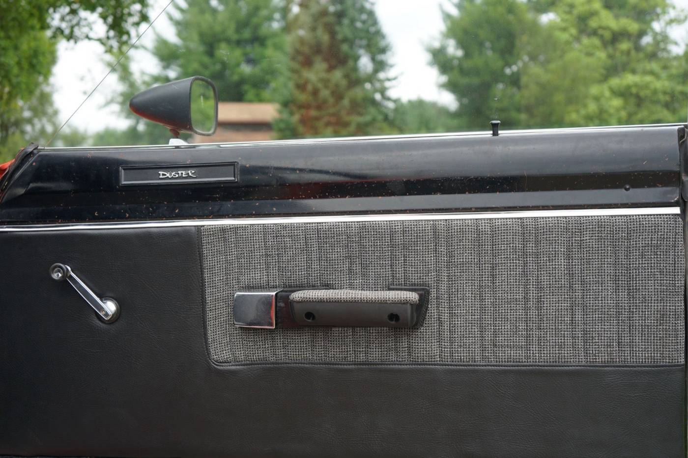 The finished door panel of a 1970s Plymouth Duster: black vinyl with a gray woven fabric insert, a chrome window crank, and a 3D printed armrest and door handle.