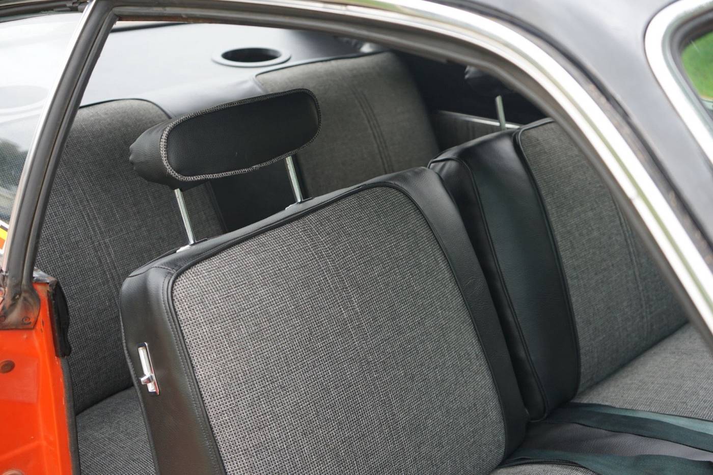 The back seat of a 1970s Plymouth Duster in black vinyl and gray woven fabric, with the custom speaker inserts made here in the rear.
